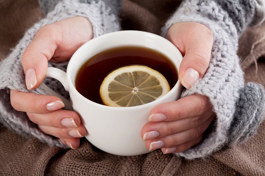 woman's hands with handwarmers on them holding a cup of tea with a slice of lemon