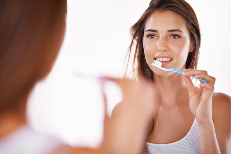 young woman looking in mirror, brushing her teeth